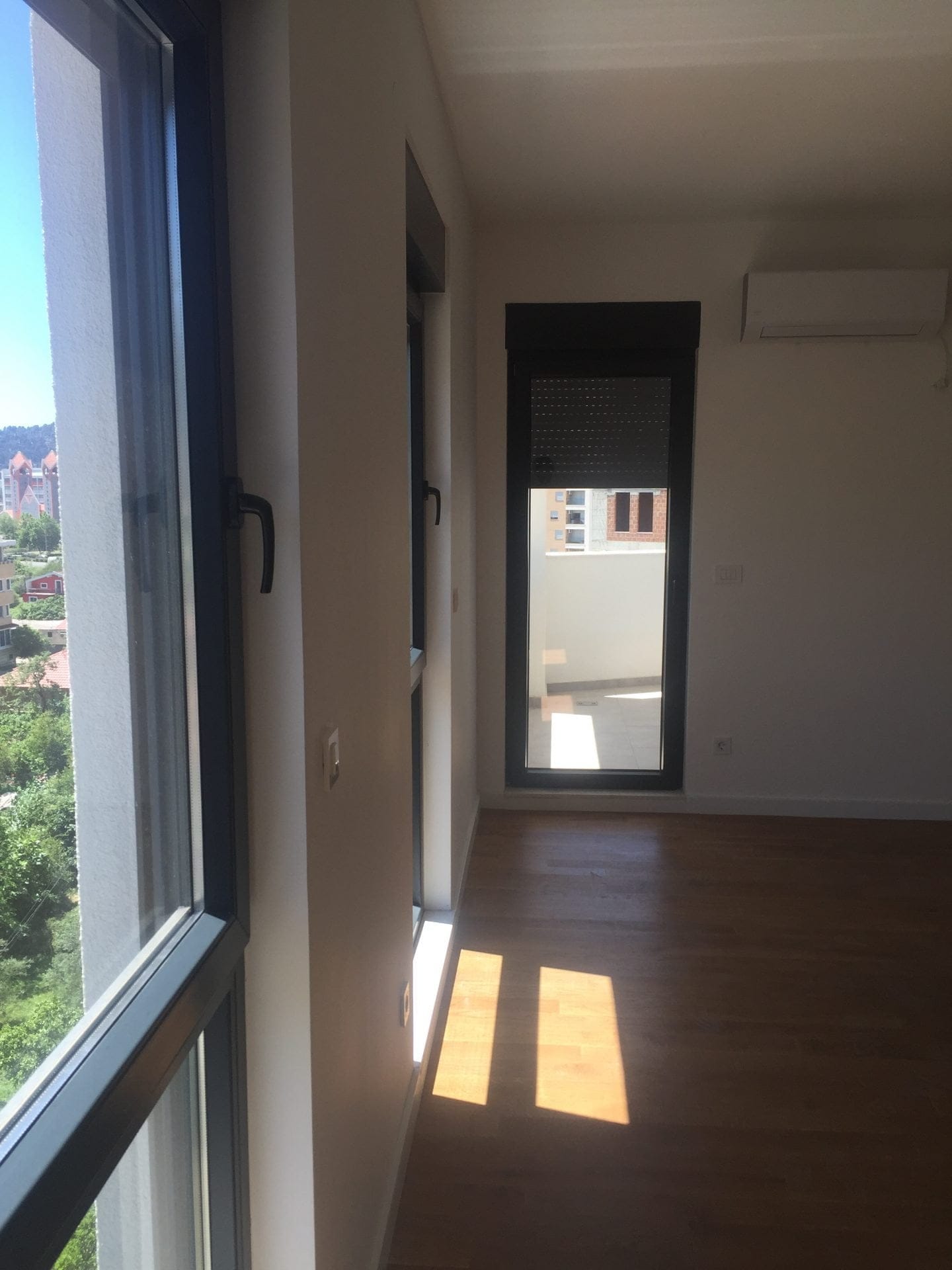 Helles Wohnzimmer mit Panoramafenstern, Parkettboden und Zugang zur Terrasse in einer neuen Wohnung, Stadt Bar, Montenegro.