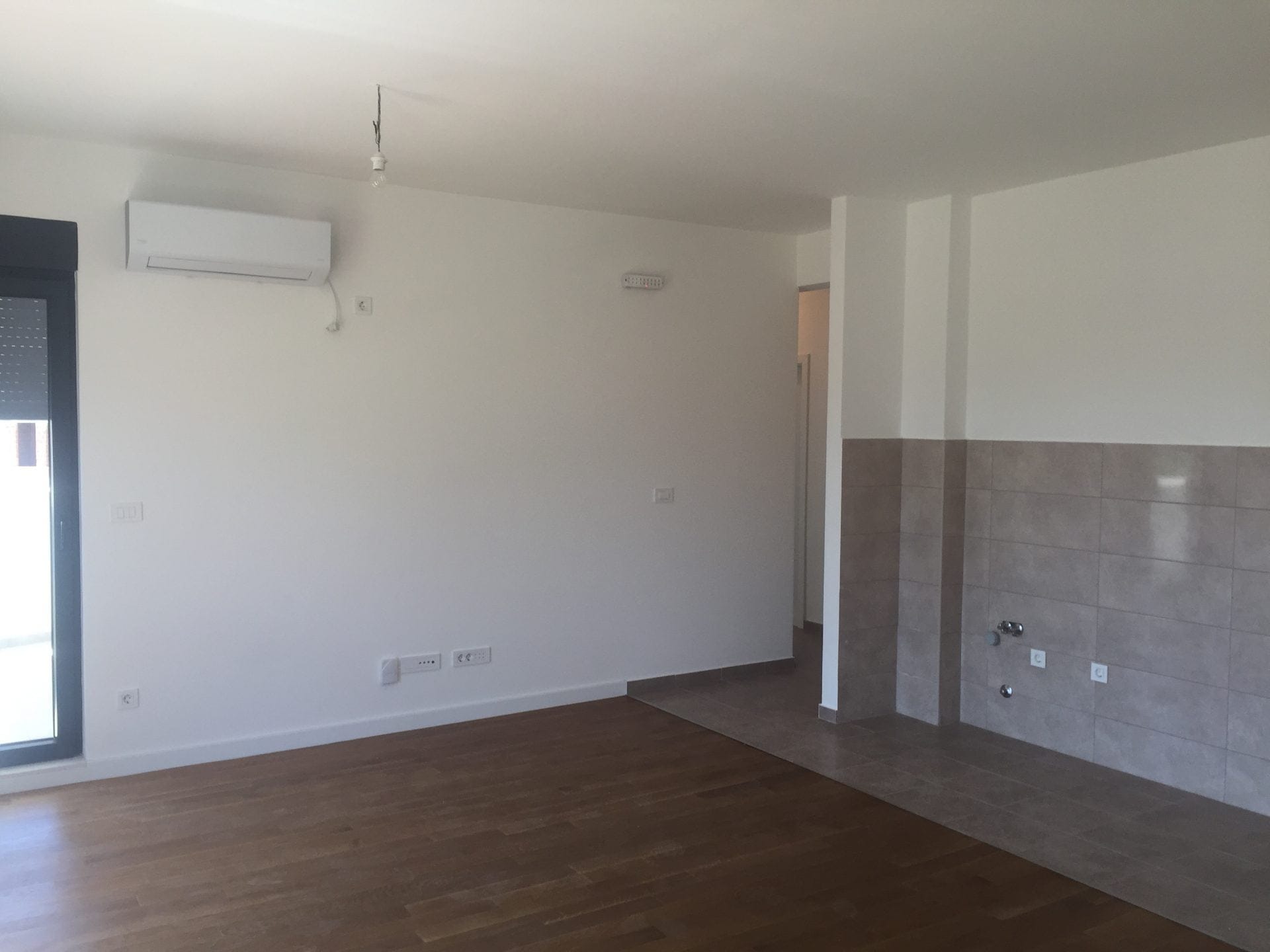 Helles Wohnzimmer mit Küchenbereich in einer neuen Wohnung in der Stadt Bar, Montenegro: Parkett, Fliesen und Klimaanlage.