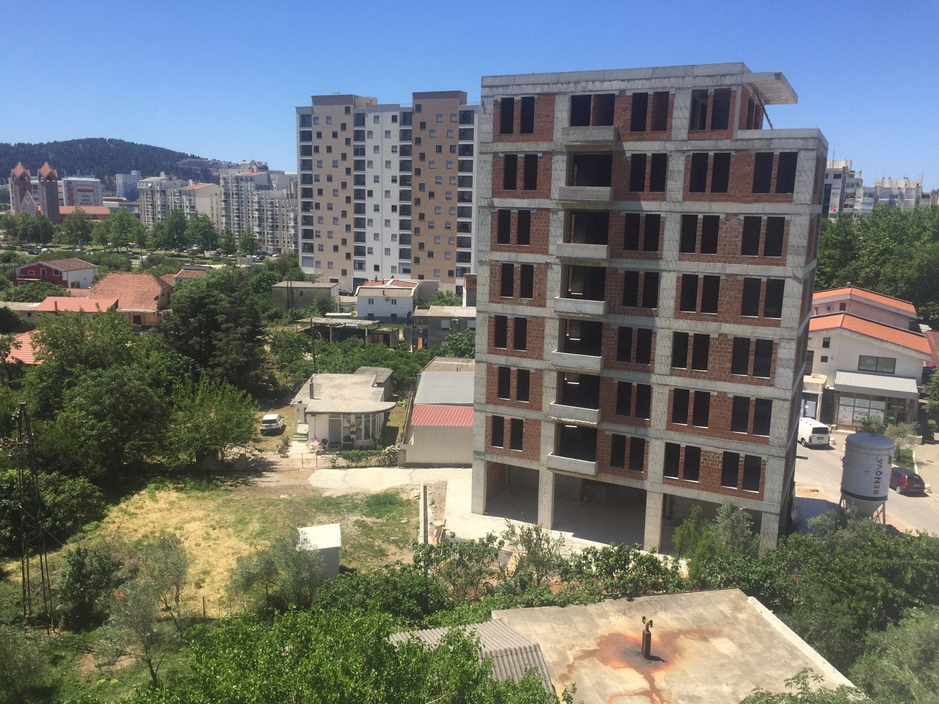 Im Bau befindliches mehrstöckiges Wohnhaus aus Ziegel und Beton in der Stadt Bar, Montenegro, mit Blick auf ein Wohngebiet und die Berge.