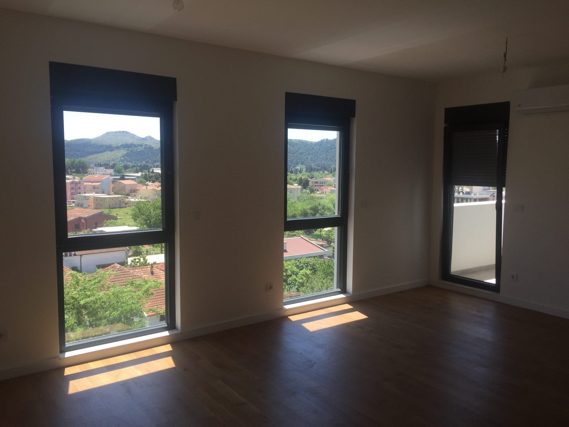 Helles Wohnzimmer in einer neuen Wohnung in Bar, Montenegro, mit Panoramafenstern, Bergblick und Parkettboden.