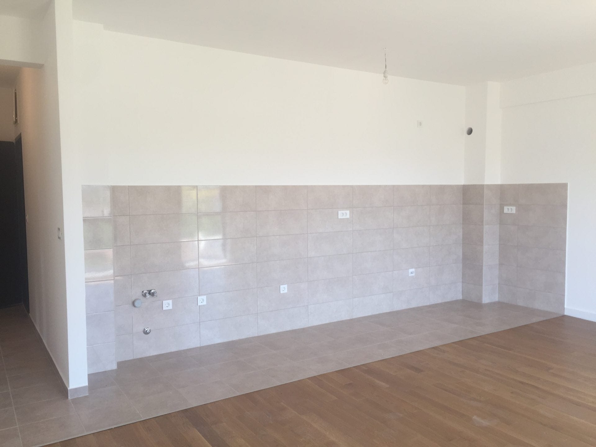 Küchenbereich in einer neuen Wohnung in Bar, Montenegro: helle Fliesen als Spritzschutz, Anschlüsse für Versorgungsleitungen und Parkettboden.