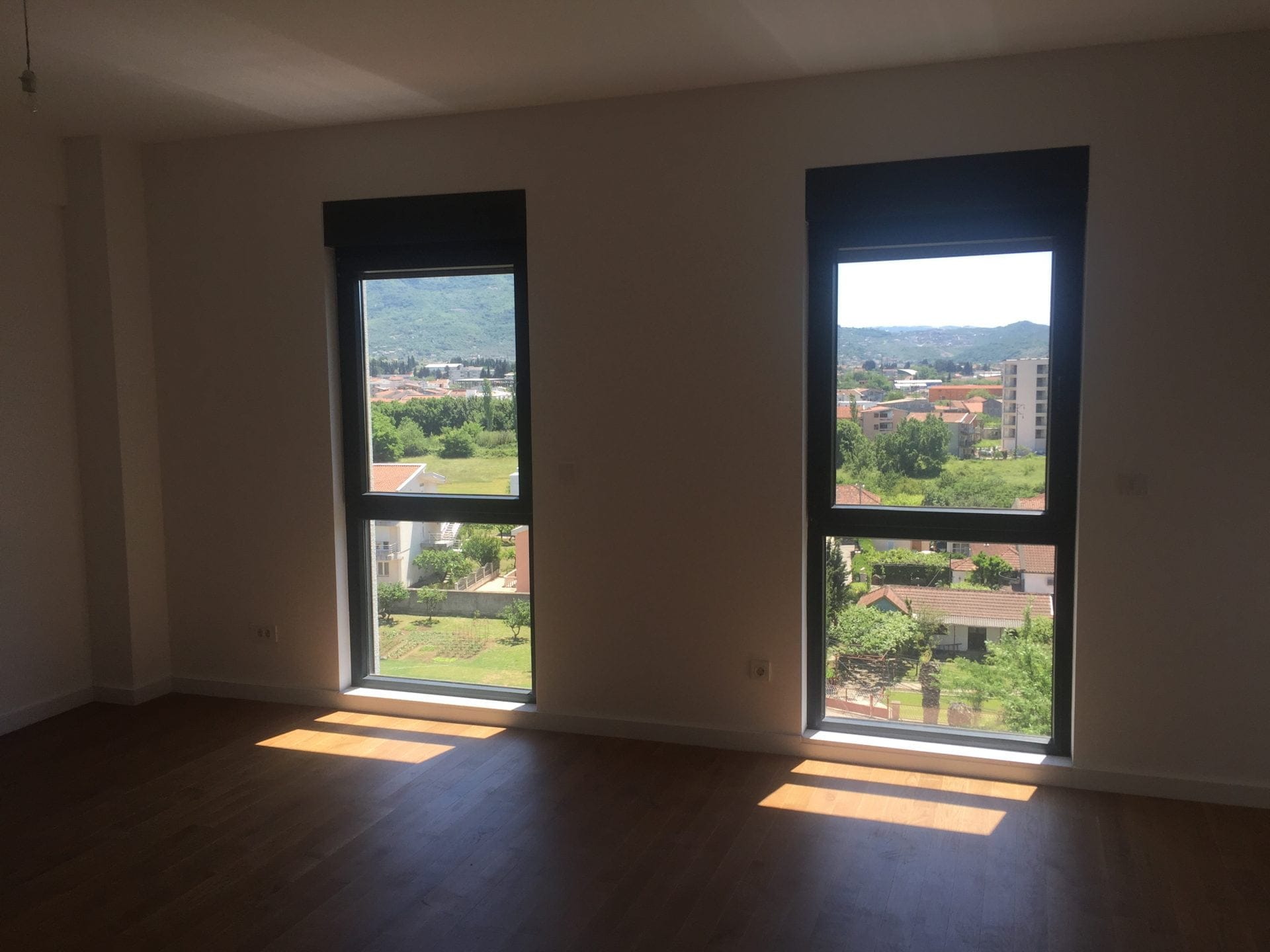 Helles Wohnzimmer mit Parkettboden und Panoramafenstern mit Blick auf die Berge und die Stadt Bar, Montenegro.