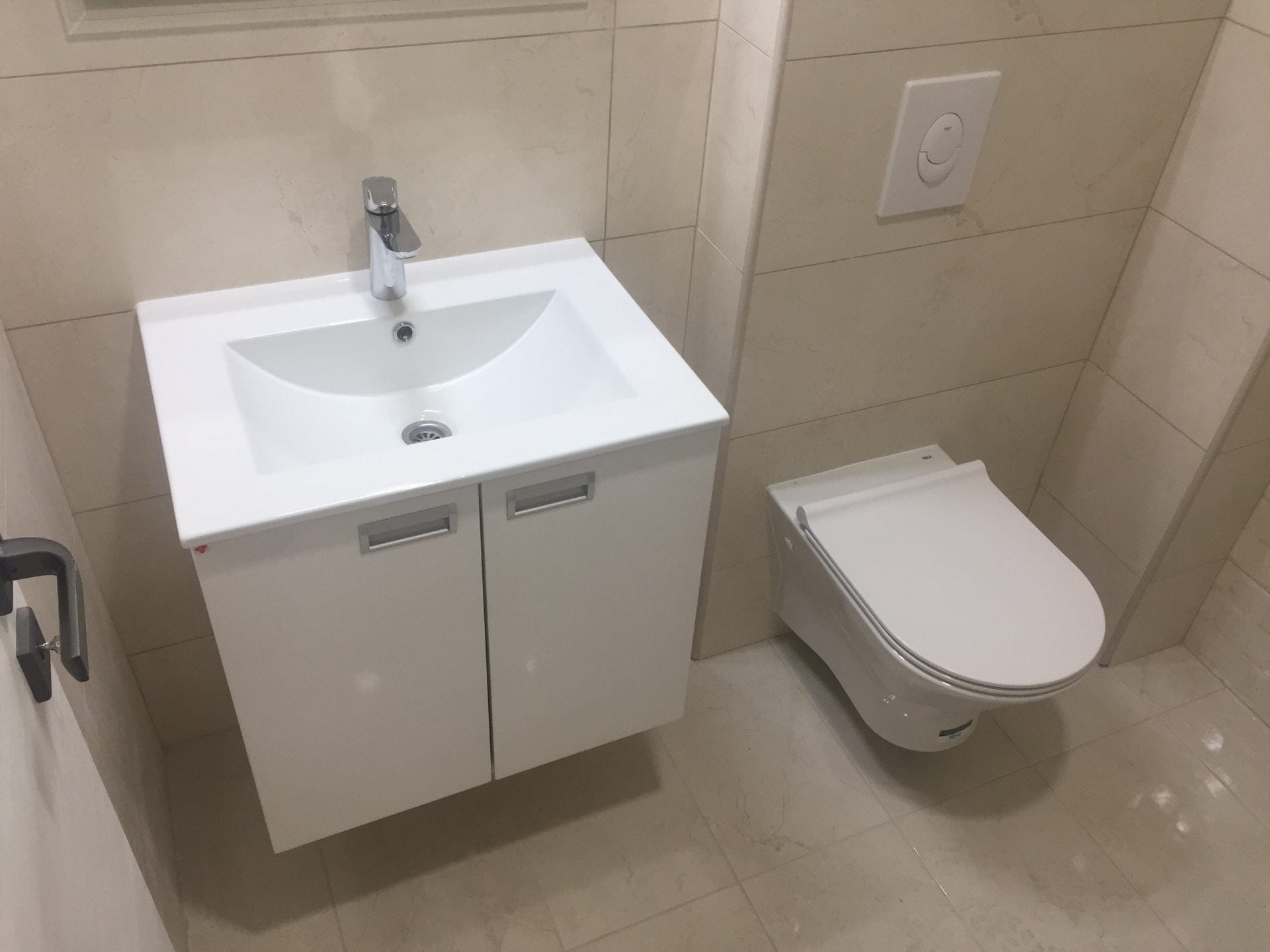 Modernes Badezimmer in einer Wohnung in Bar, Montenegro: weiße Waschtischanlage mit Waschbecken und wandhängendes WC, beige Fliesen.