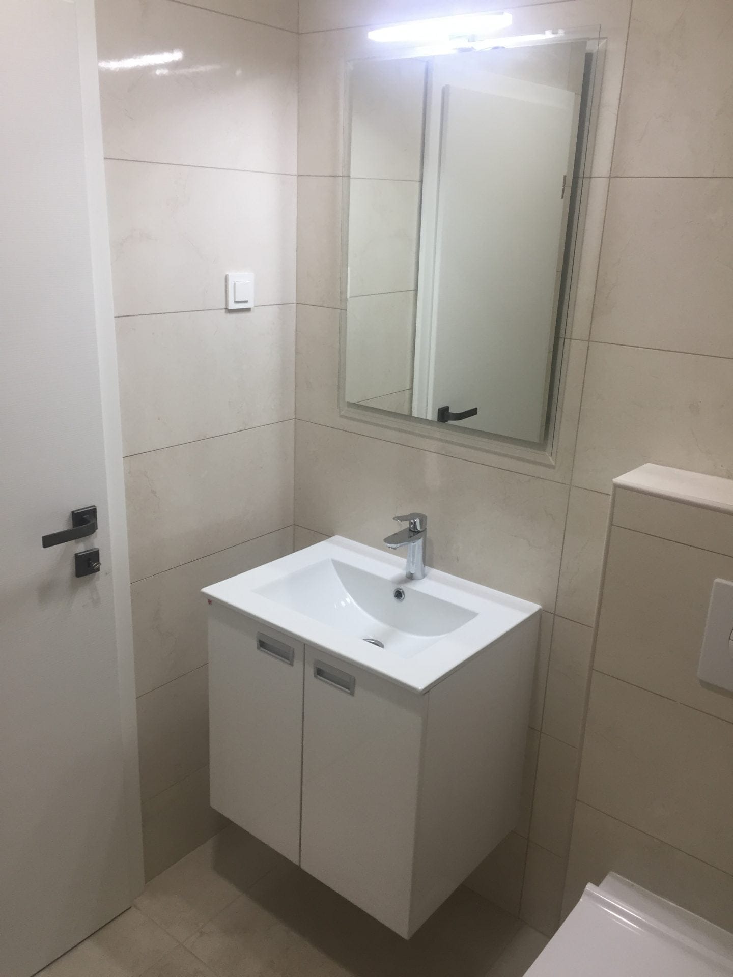 Modernes Badezimmer in einer Wohnung, Stadt Bar, Montenegro: weiße Waschtischkonsole mit Waschbecken, Spiegel und helle Fliesen.