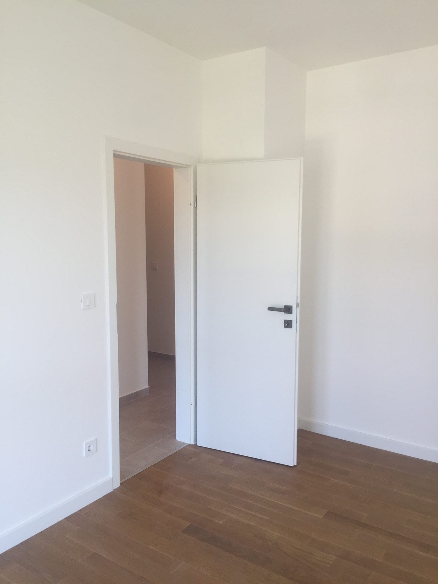 Moderne Wohnung in Bar, Montenegro: heller Raum mit weißen Wänden, Innentür und Parkettboden.