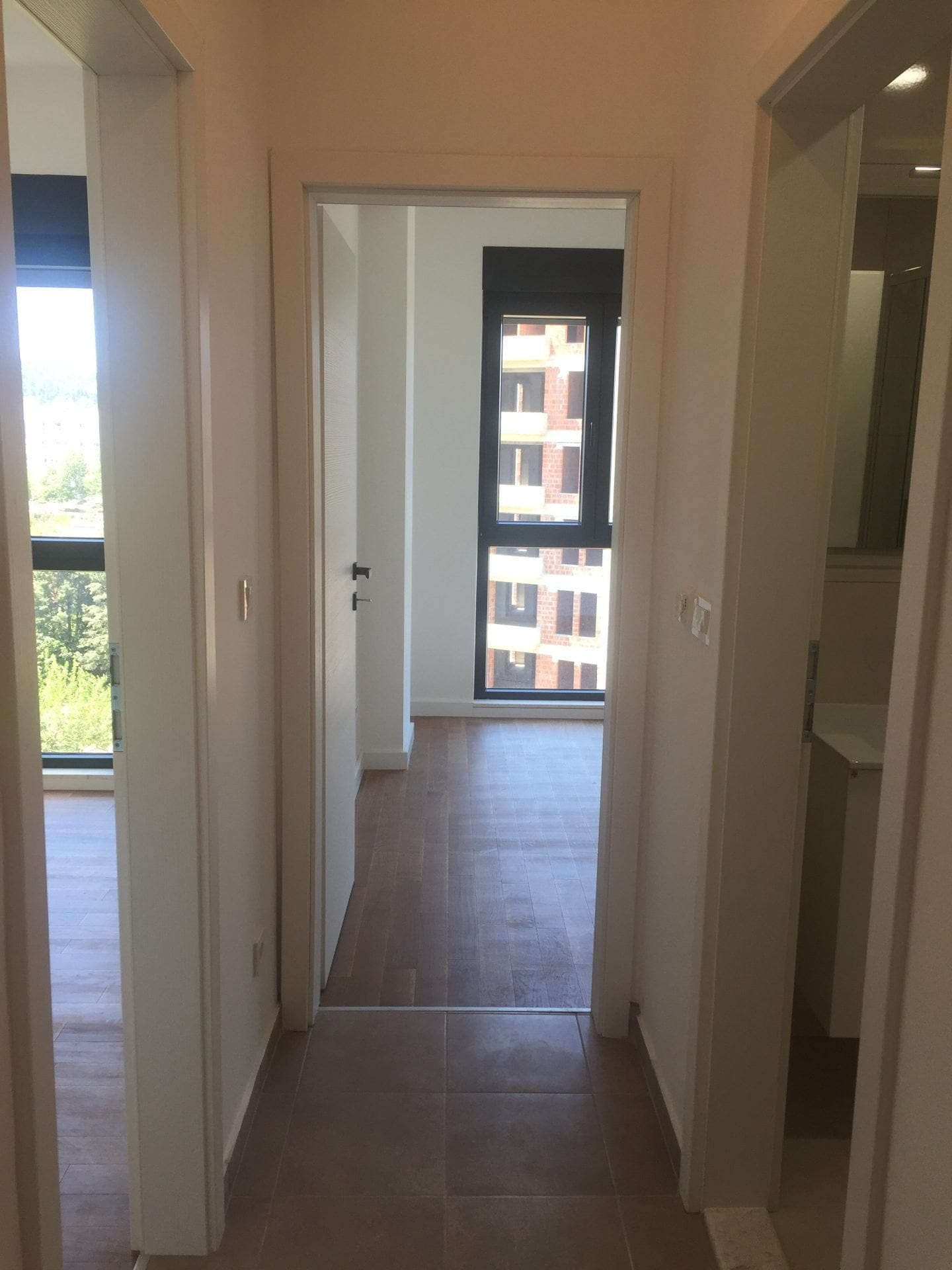 Heller Flur in einer neuen Wohnung in Bar, Montenegro: Laminat, Innentüren und Blick aus dem Fenster auf das Nachbarhaus.
