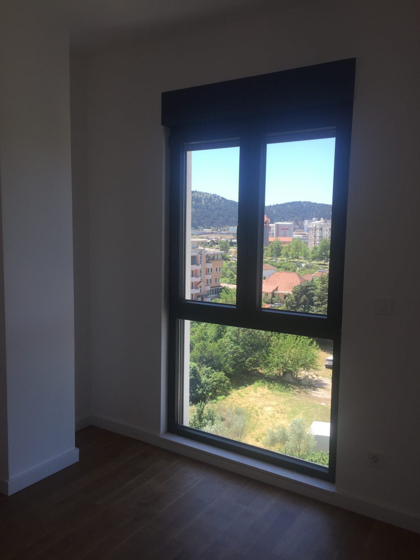 Blick aus dem Schlafzimmerfenster in einer Wohnung in der Stadt Bar, Montenegro: Panoramafenster, helle Ausstattung und Holzboden.