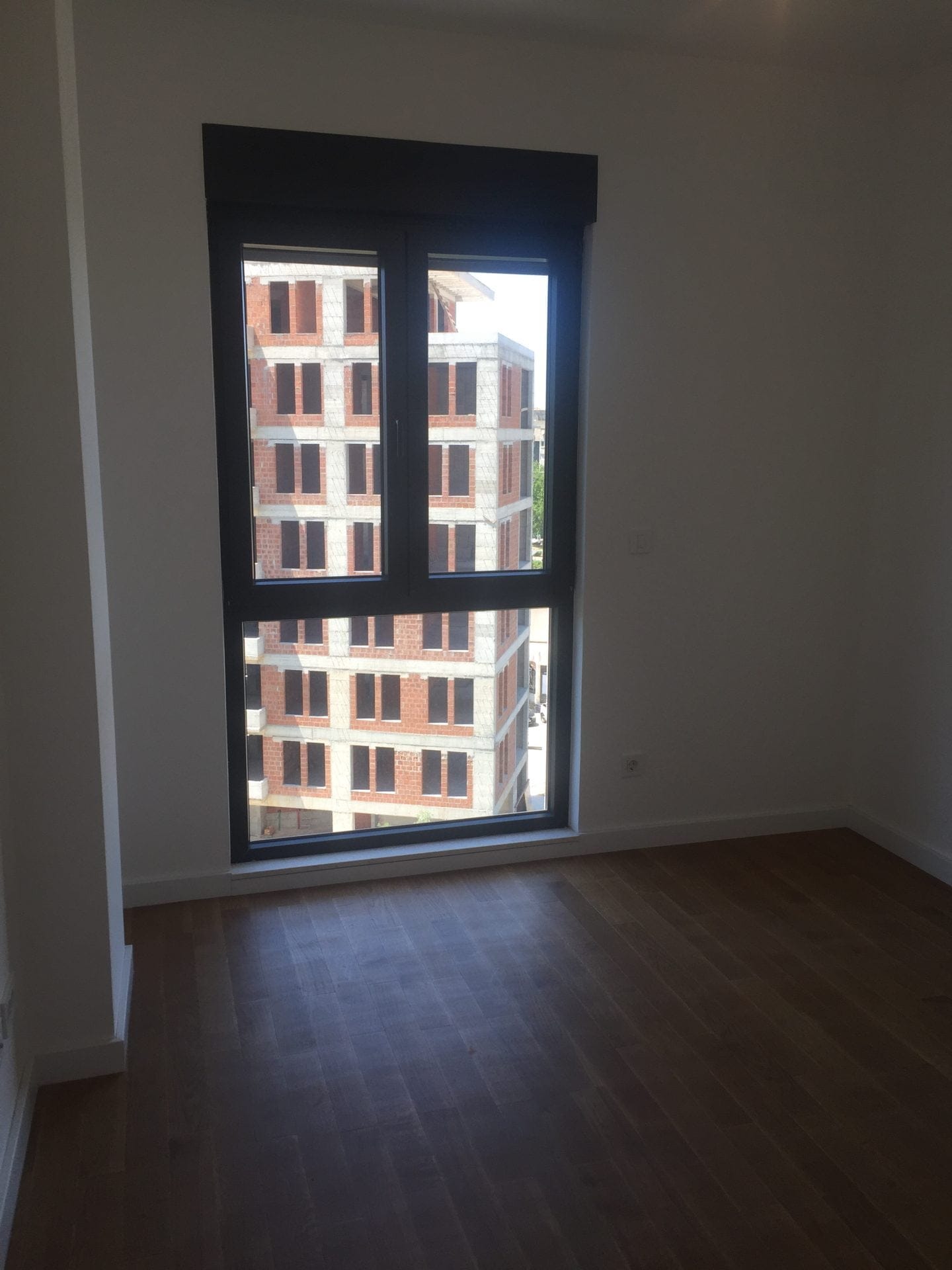 Schlafzimmer in einer neuen Wohnung in Bar, Montenegro: helle Ausstattung, Parkettboden und Blick aus dem Fenster auf ein im Bau befindliches Haus.