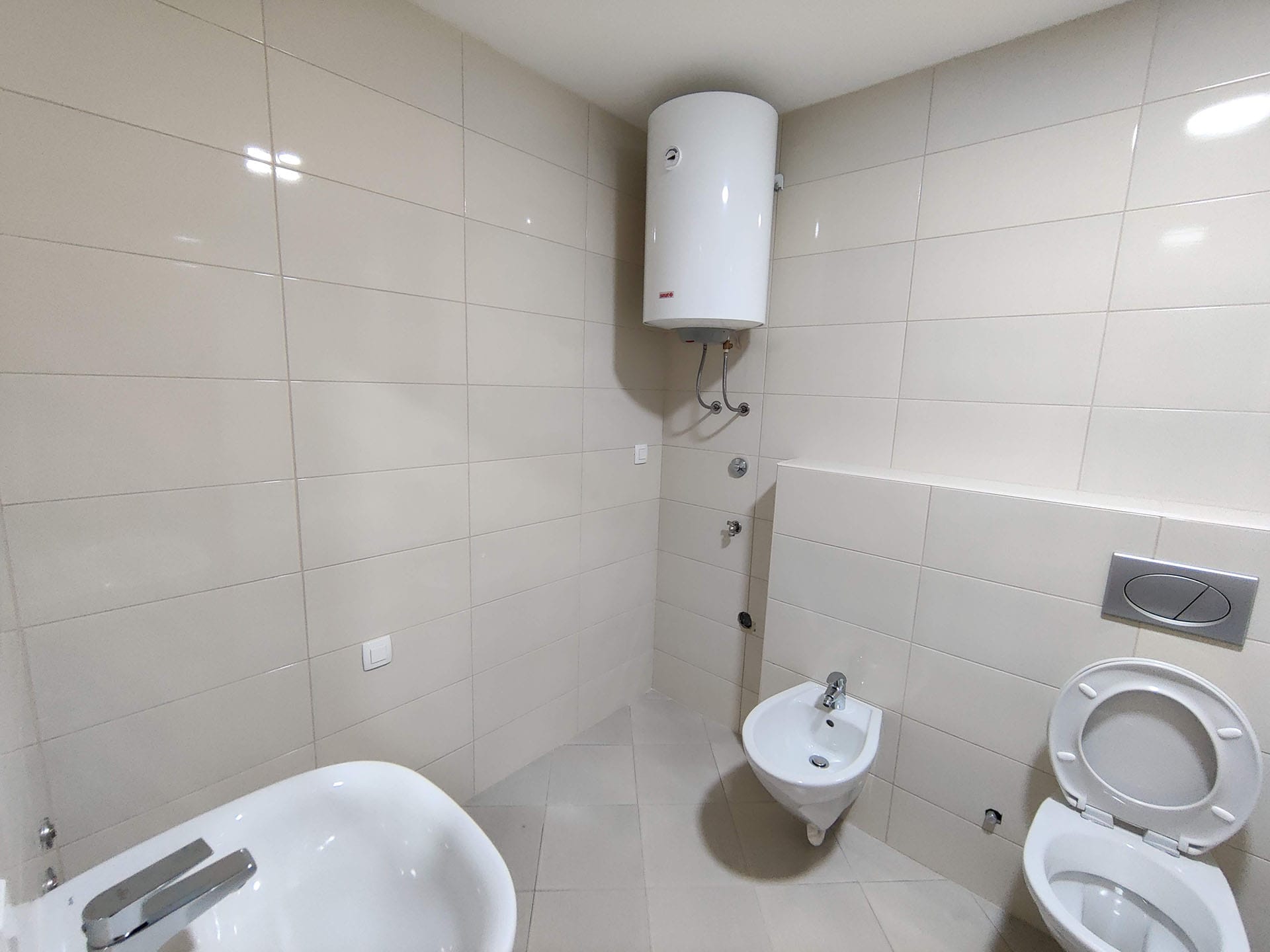 Salle de bain lumineuse dans un appartement à Bečići, Monténégro : sanitaires, bidet, toilettes et chauffe-eau mural.