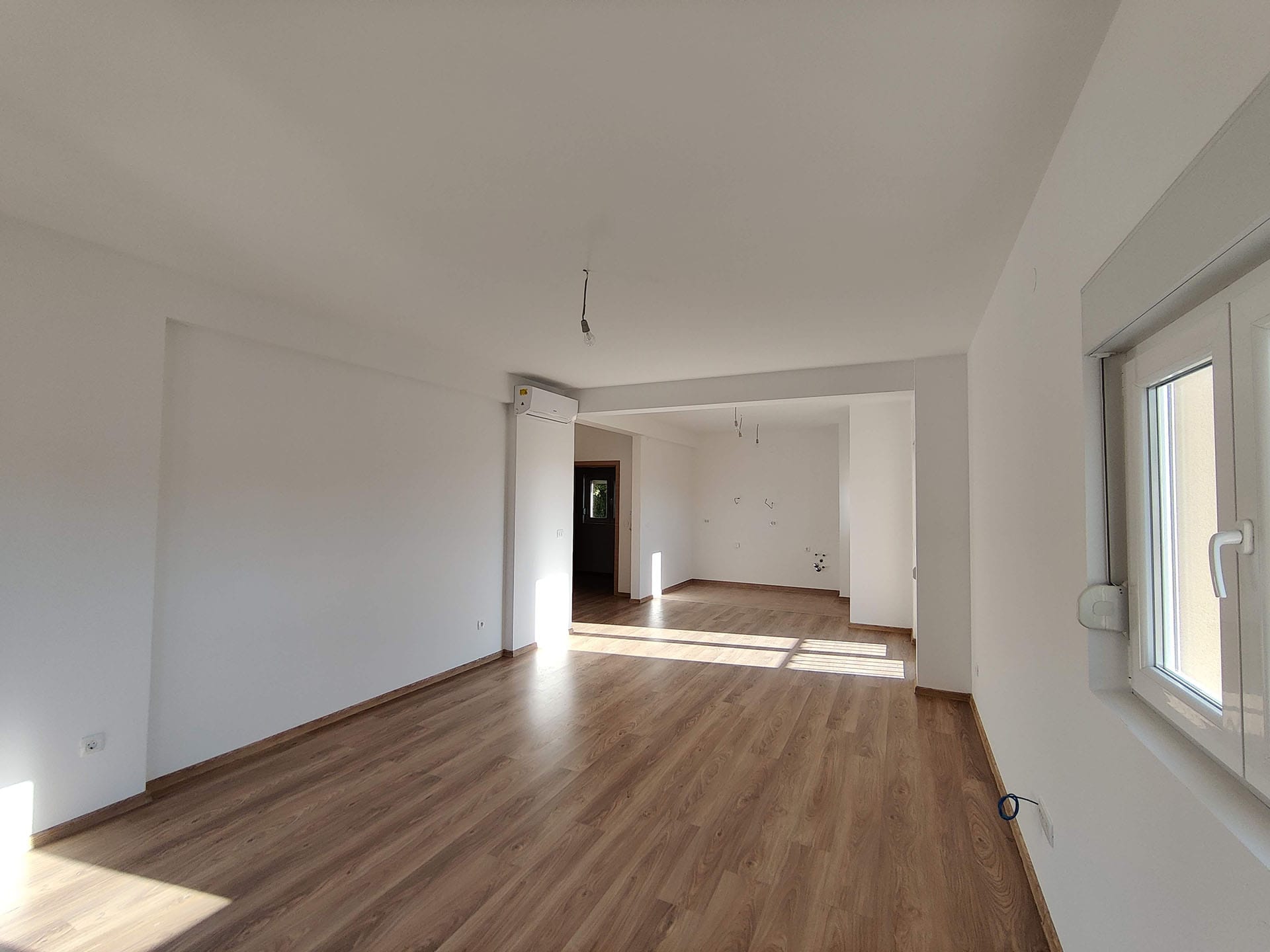 Salon lumineux avec parquet stratifié dans un nouvel appartement à Bečići, Monténégro : finition soignée, climatisation et fenêtres en PVC.
