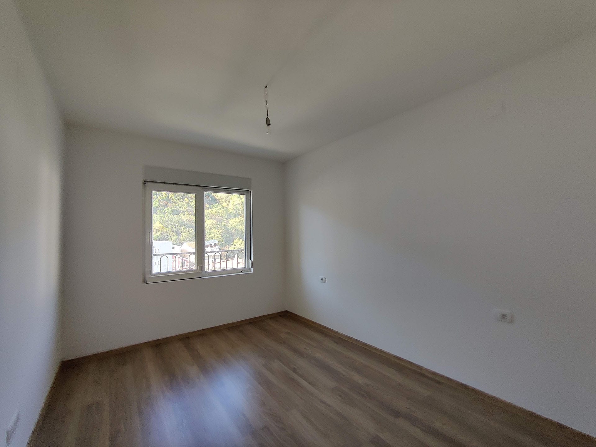 Chambre lumineuse avec parquet stratifié et vue sur les montagnes dans un appartement, Bečići, Monténégro. Pièce vide à finir.