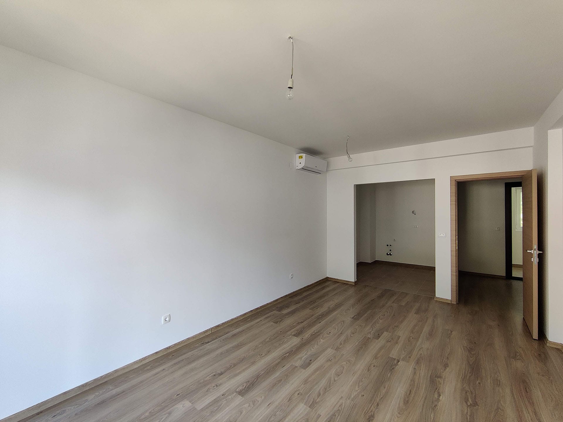 Salon lumineux avec parquet stratifié et climatisation dans un nouvel appartement à Bečići, Monténégro, vue sur la cuisine et le couloir.