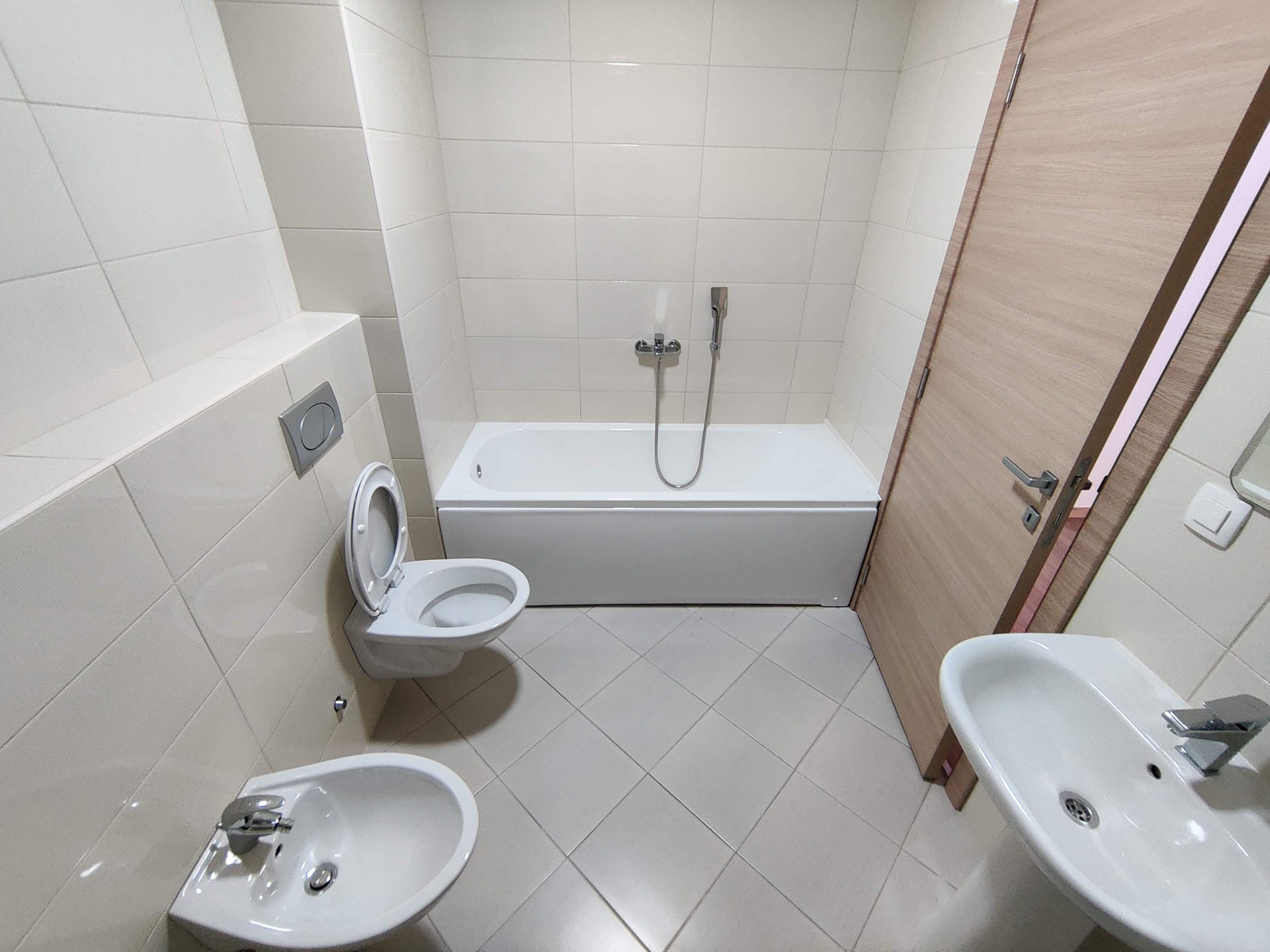 Salle de bain lumineuse dans un appartement à Bečići, Monténégro : baignoire, WC suspendu, bidet et finition moderne en carrelage.