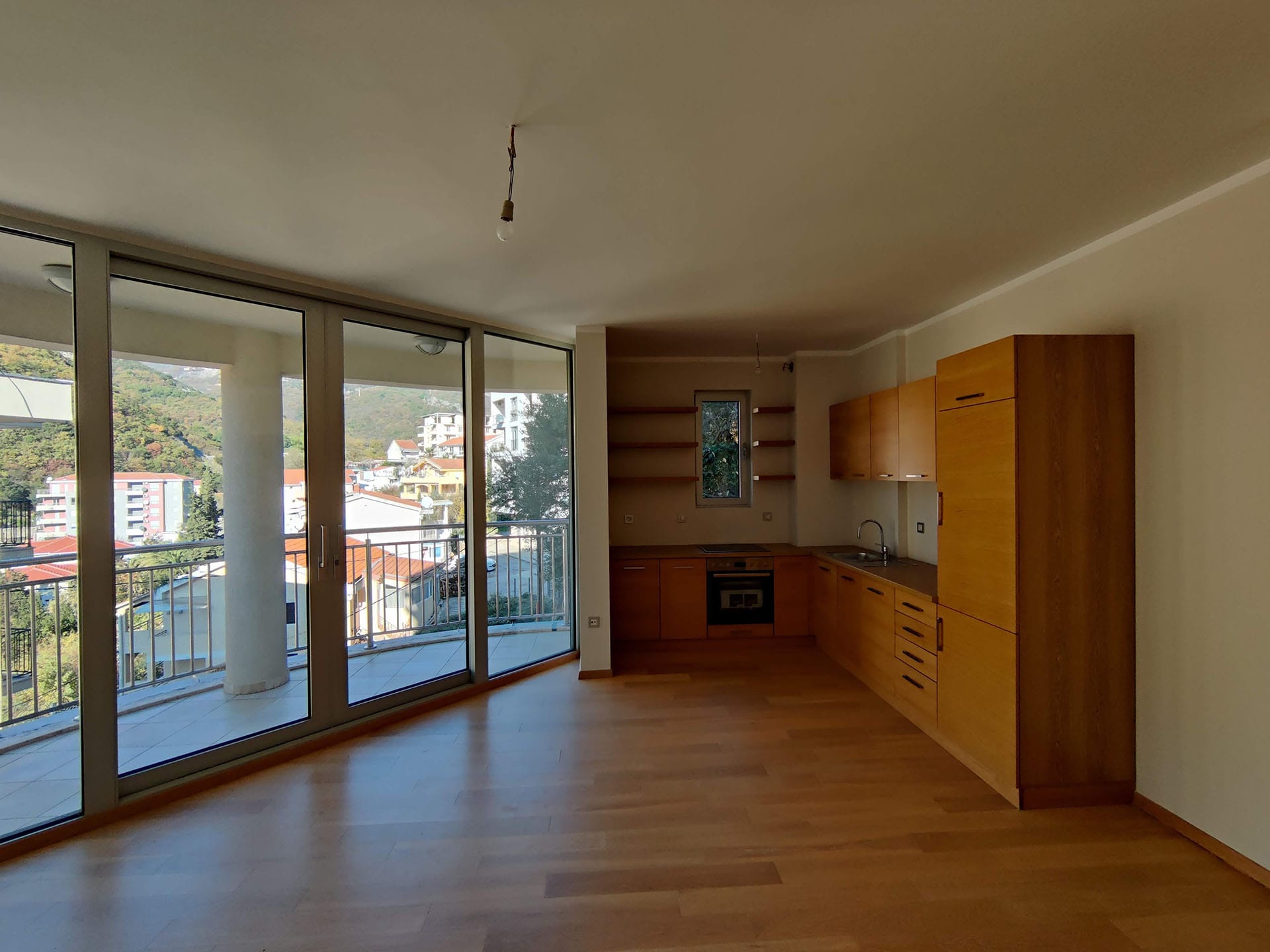 Cuisine avec mobilier en bois et fenêtres panoramiques dans un appartement à Bečići, Monténégro, avec vue sur les montagnes et la ville.