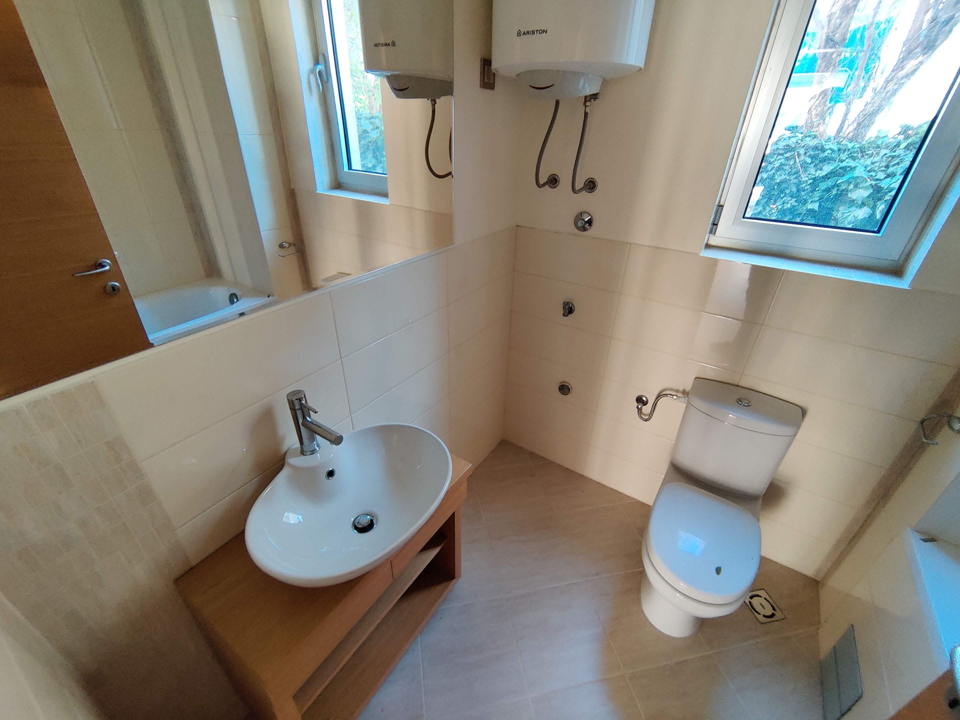 Salle de bains lumineuse dans un appartement à Bečići, Monténégro : lavabo sur meuble en bois, toilettes et chauffe-eau Ariston.