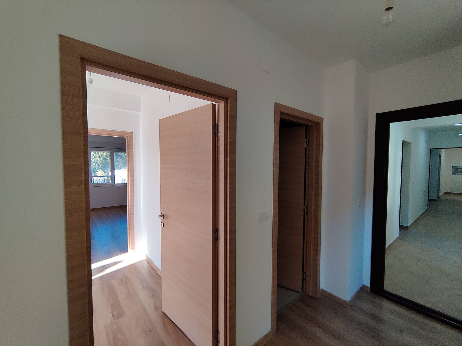 Couloir lumineux avec portes intérieures imitation bois dans un appartement, Bečići, Monténégro. Vue sur les pièces attenantes.