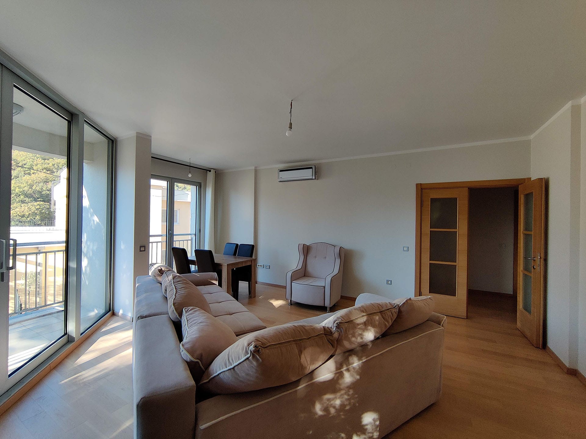 Salon lumineux avec baies vitrées panoramiques et mobilier dans un appartement à Bečići, Monténégro. Parquet, coin repas et balcon.