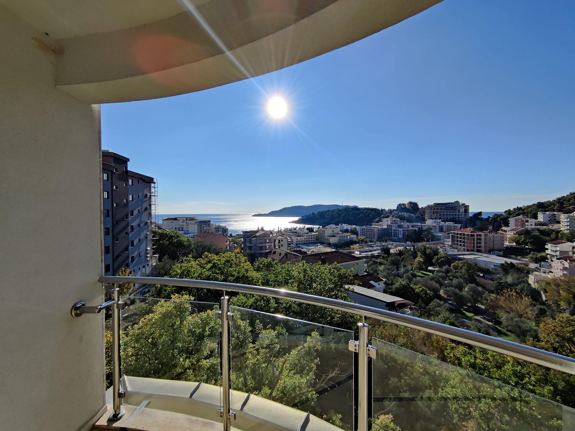 Vue depuis le balcon d’un appartement à Bečići, Monténégro : panorama de la ville, collines verdoyantes et mer Adriatique par une journée ensoleillée.