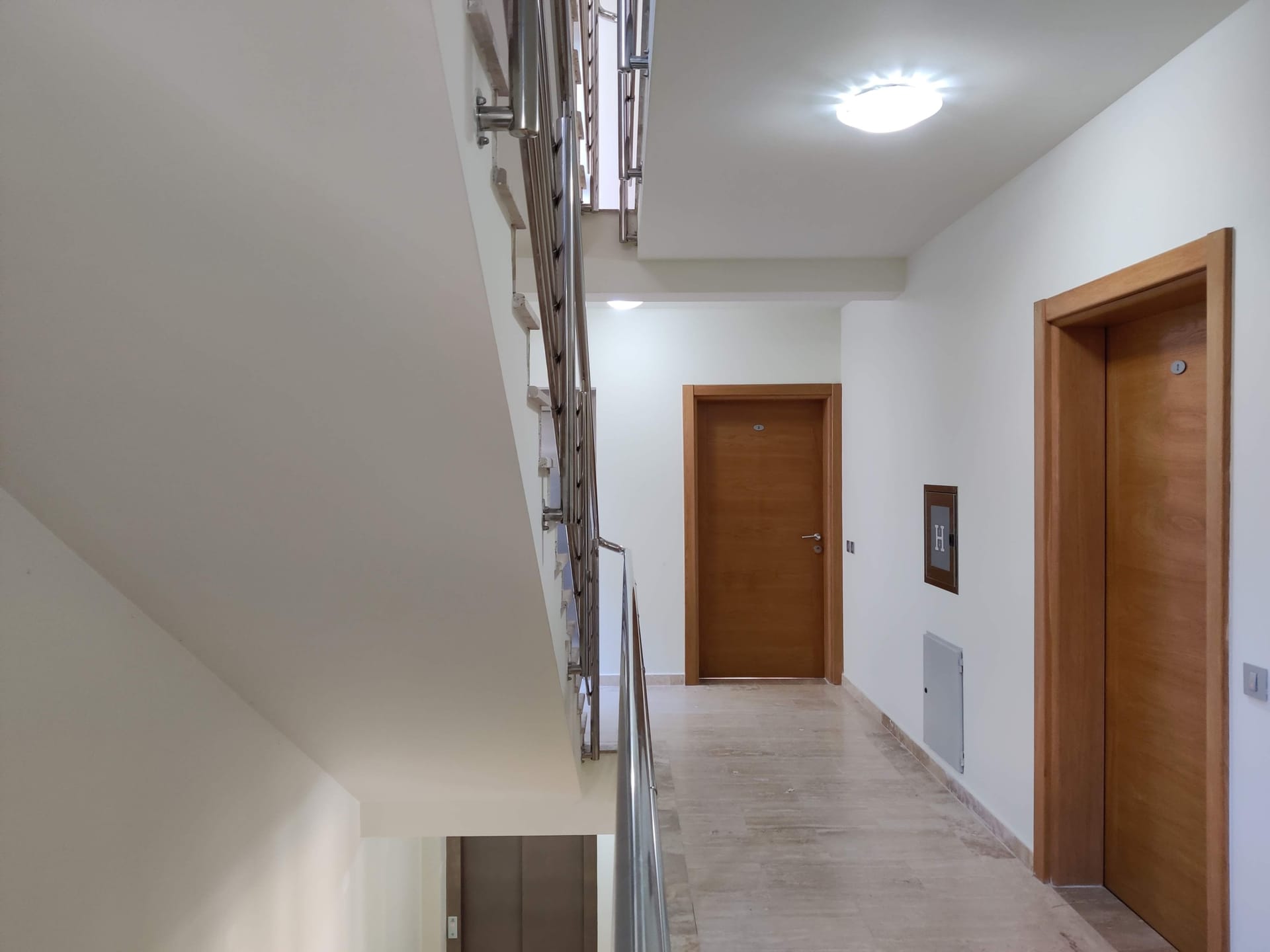 Couloir lumineux et escalier avec rampe métallique dans un complexe résidentiel à Bečići, Monténégro. Portes intérieures en bois.