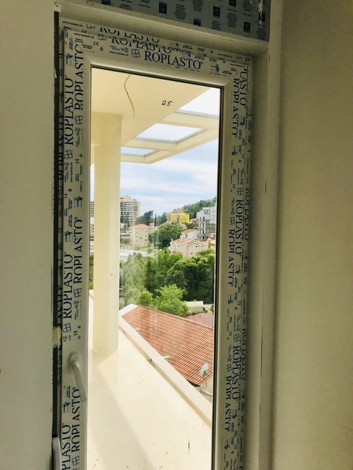 Vue depuis le balcon sur la ville de Bečići au Monténégro à travers une nouvelle fenêtre en PVC à double vitrage Roplasto dans un immeuble en construction.