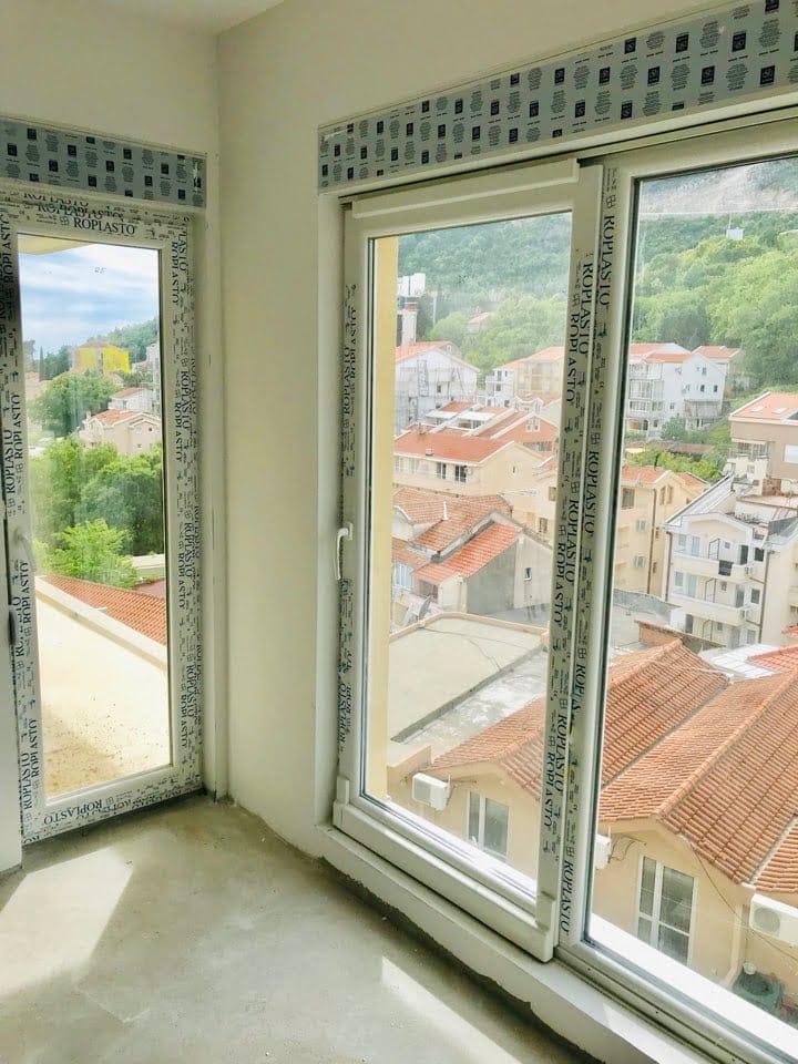 Vue depuis la fenêtre du salon sur les toits en tuiles et les montagnes à Bečići, Monténégro. Nouvelles fenêtres en plastique dans un appartement lumineux.