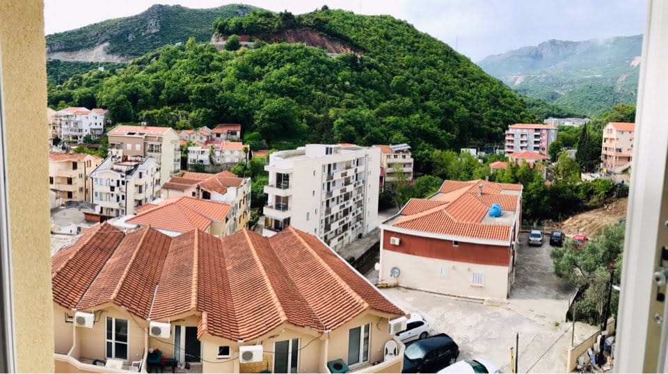 Vue depuis le balcon d’un appartement à Bečići, Monténégro : panorama sur des immeubles résidentiels aux toits de tuiles et des montagnes verdoyantes.