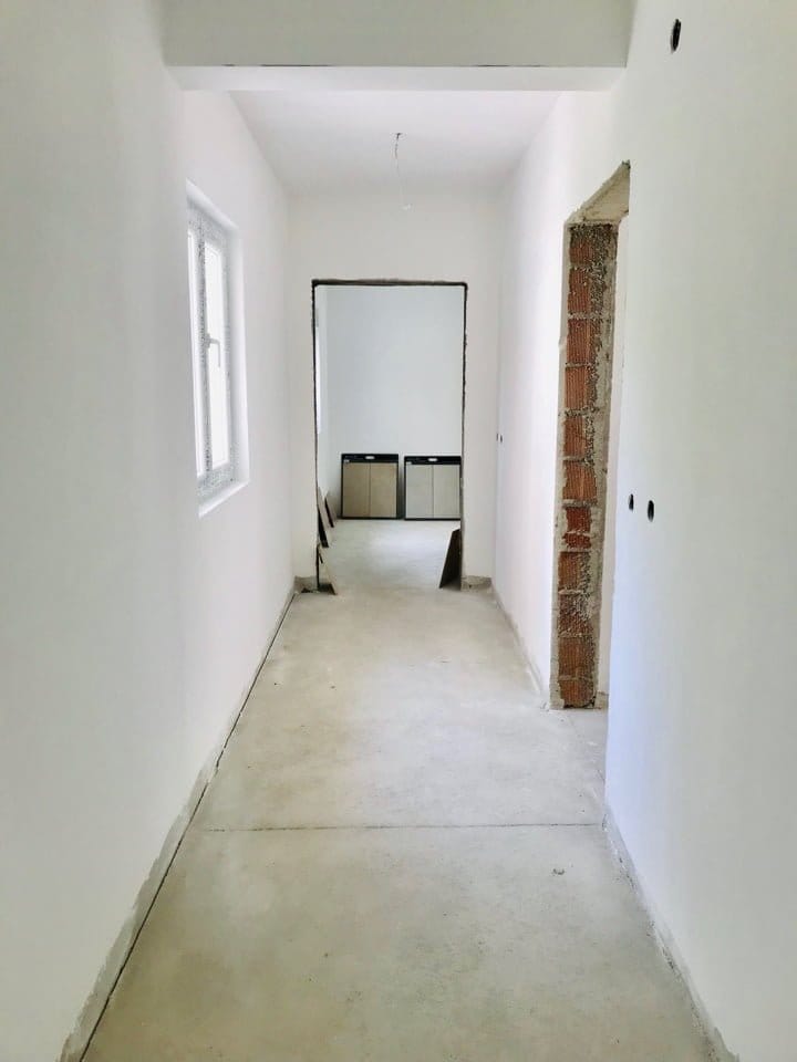 Couloir dans un appartement en construction à Bečići, Monténégro : murs blancs, sol en béton et ouverture vers la pièce voisine.