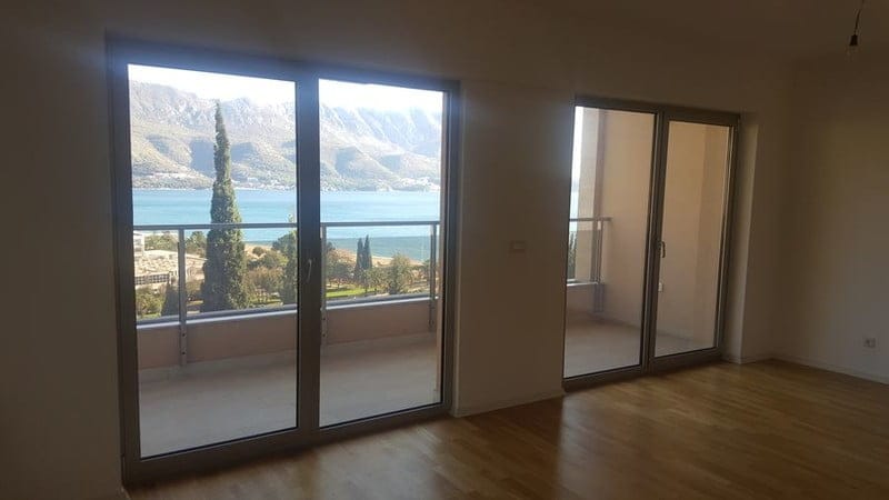 Dnevna soba sa panoramskim prozorima i pogledom na more i planine u stanu, Bečići, Crna Gora. Parketni pod, izlaz na balkon.