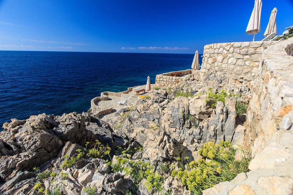 Terrasse mit Steinverkleidung und Sonnenschirmen am Meer in einer Wohnanlage, Dobre Vode, Montenegro, Blick auf die Adriaküste