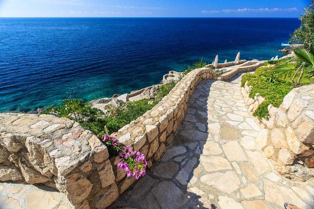 Steinweg zum Meer in einer Wohnanlage, Dobre Vode, Montenegro: Blick auf die Küste und das azurblaue Wasser.