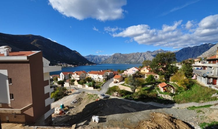 Panoramski pogled na Bokokotorski zaliv i planine iz stana u Dobroti, Crna Gora: stambeni deo sa kućama i morskim pejzažom.