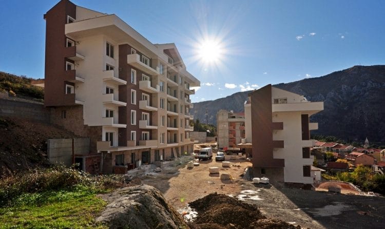 Savremeni stambeni kompleks u Dobroti, Crna Gora: višespratnice u izgradnji sa balkonima u pozadini planina.