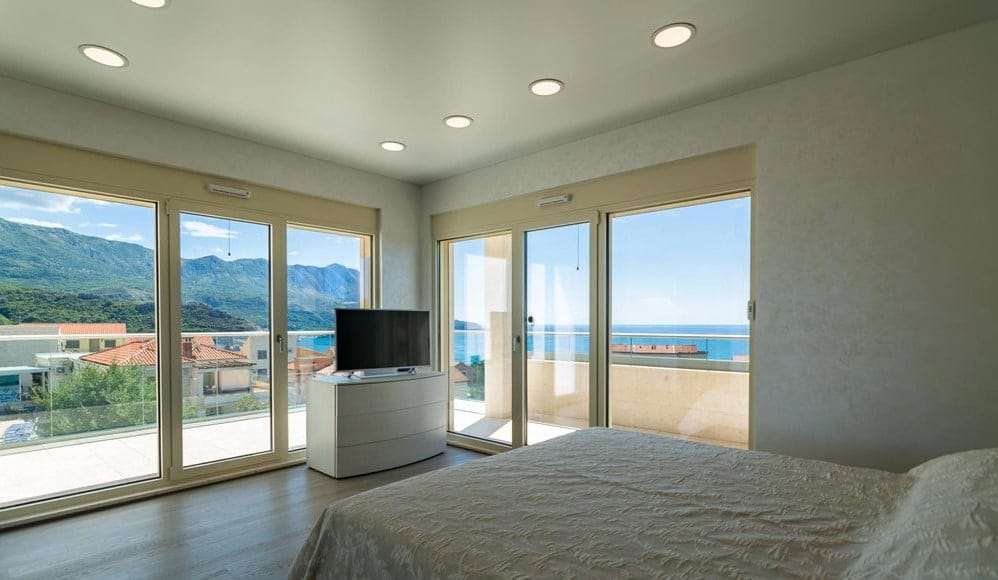 Becici, Karadağ’daki villada deniz ve dağ manzaralı panoramik pencereli yatak odası. TV alanına sahip modern iç mekan.