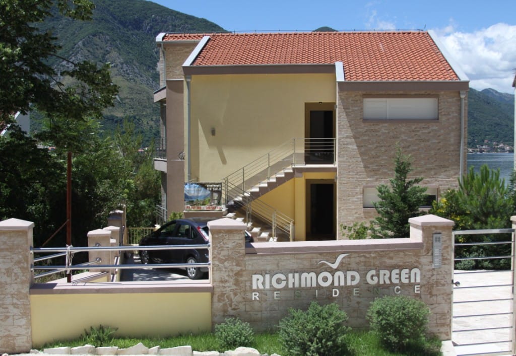 Fassade des Wohnkomplexes Richmond Green in Dobrota, Montenegro: modernes Gebäude mit Steinverkleidung und Blick auf die Berge.