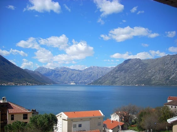 Panoramablick auf die Bucht von Kotor und die Berge aus einer Wohnung in Dobrota, Montenegro: Häuser mit Ziegeldächern und das Meer.