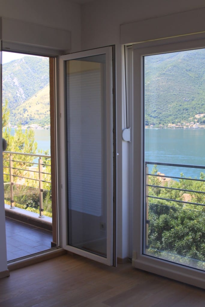 Blick vom Wohnzimmer auf die Bucht von Kotor und die Berge in einer Wohnung in Dobrota, Montenegro: Panoramafenster und Zugang zum Balkon.