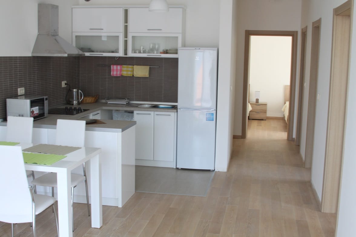 Moderne Küche mit weißen Möbeln und Essbereich in einer Wohnung in Dobrota, Montenegro. Blick auf den Flur und das Schlafzimmer.