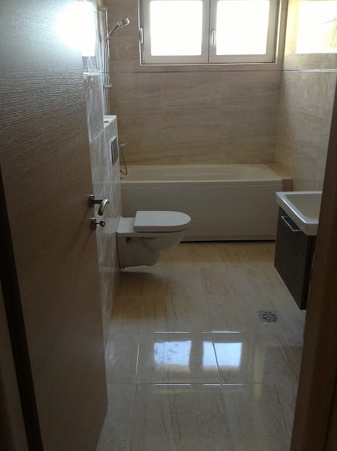Modernes Badezimmer in einer Wohnung in Dobrota, Montenegro: beige Fliesen, Badewanne, Hänge-WC und Waschtisch mit Waschbecken.