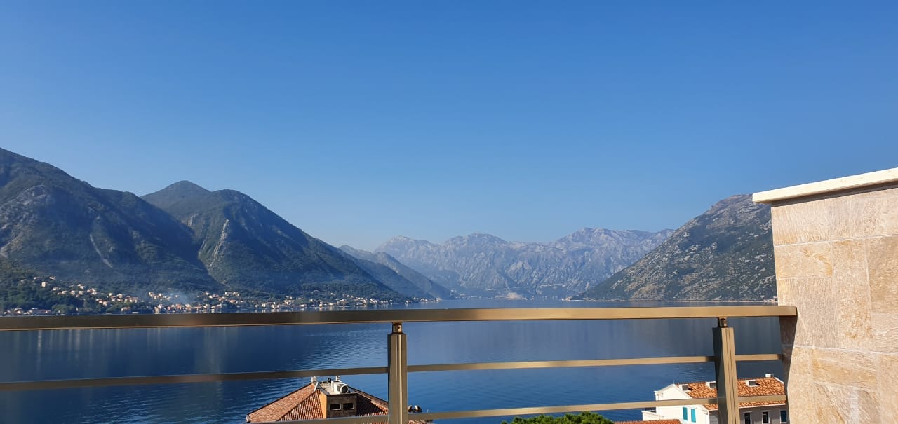 Panoramablick auf die Bucht von Kotor und die Berge vom Balkon der Wohnung in Dobrota, Montenegro, mit modernem Metallgeländer.