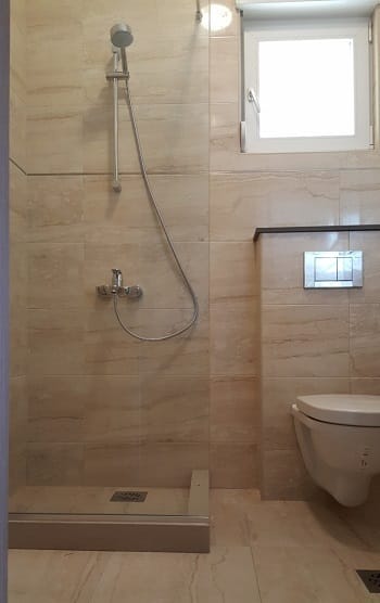 Modernes Badezimmer in einer Wohnung, Dobrota, Montenegro: Duschkabine, wandhängendes WC und beige Fliesen.