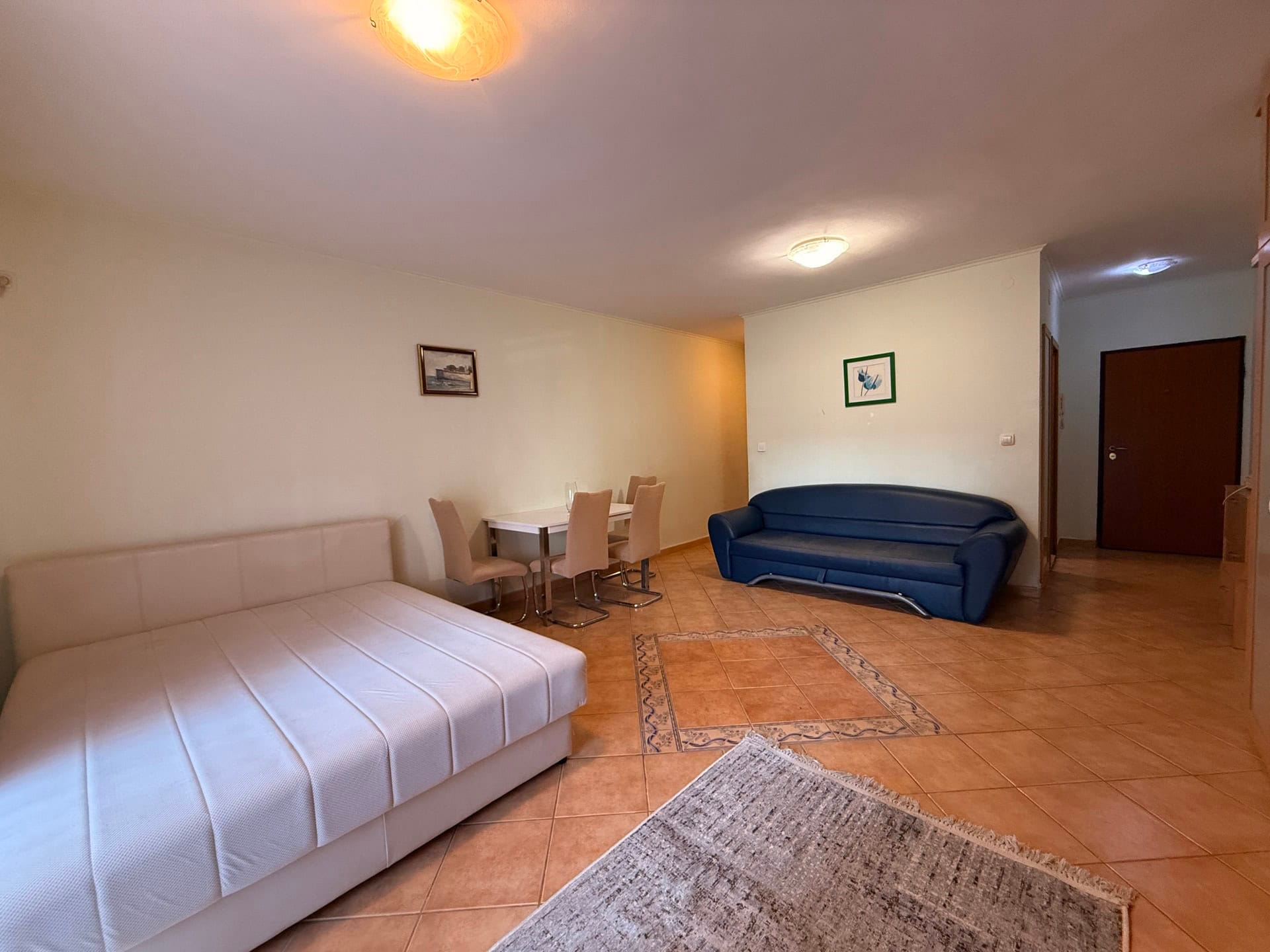 Living room in an apartment in Budva, Montenegro: a bright room with a double bed, a blue sofa, and a dining area.