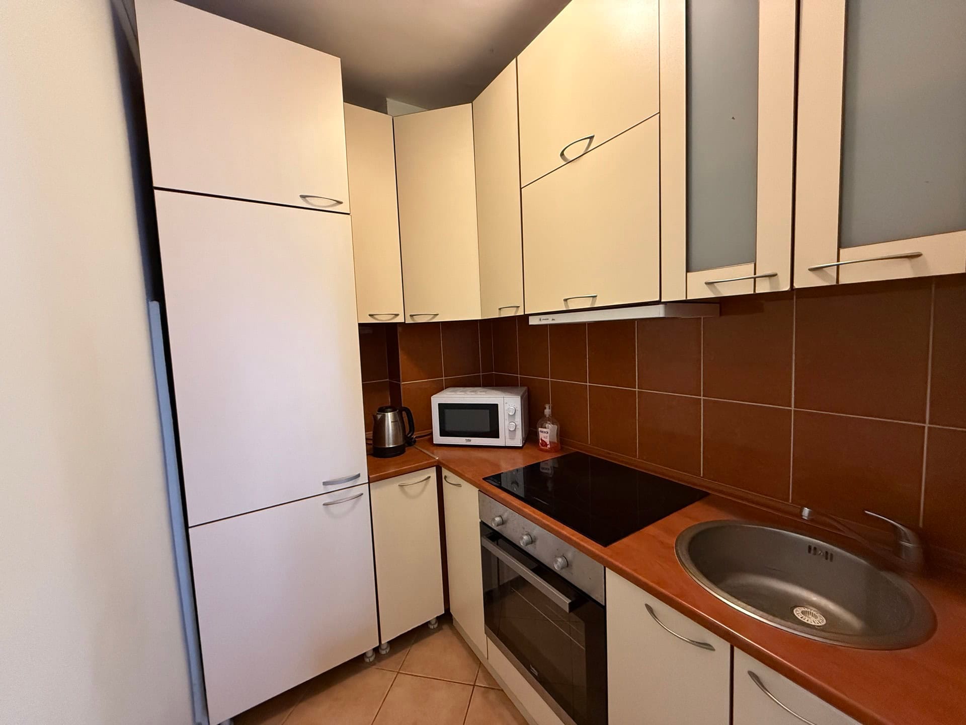 Bright corner kitchen in an apartment in Budva, Montenegro: built-in appliances, stove, sink, and a brown backsplash.
