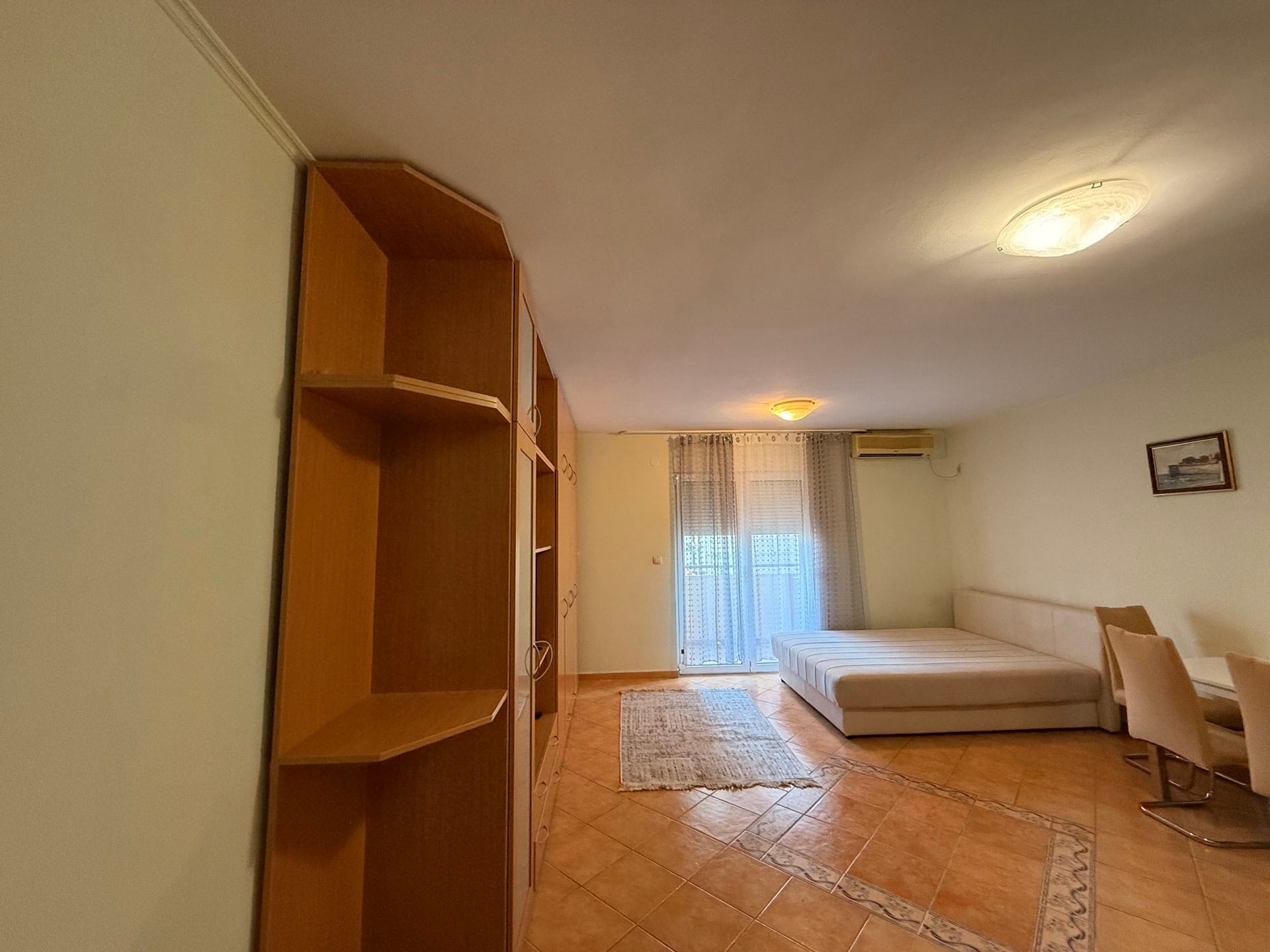 Living room in an apartment in Budva, Montenegro: a bright room with tile flooring, a large wardrobe, a bed, and access to the balcony.
