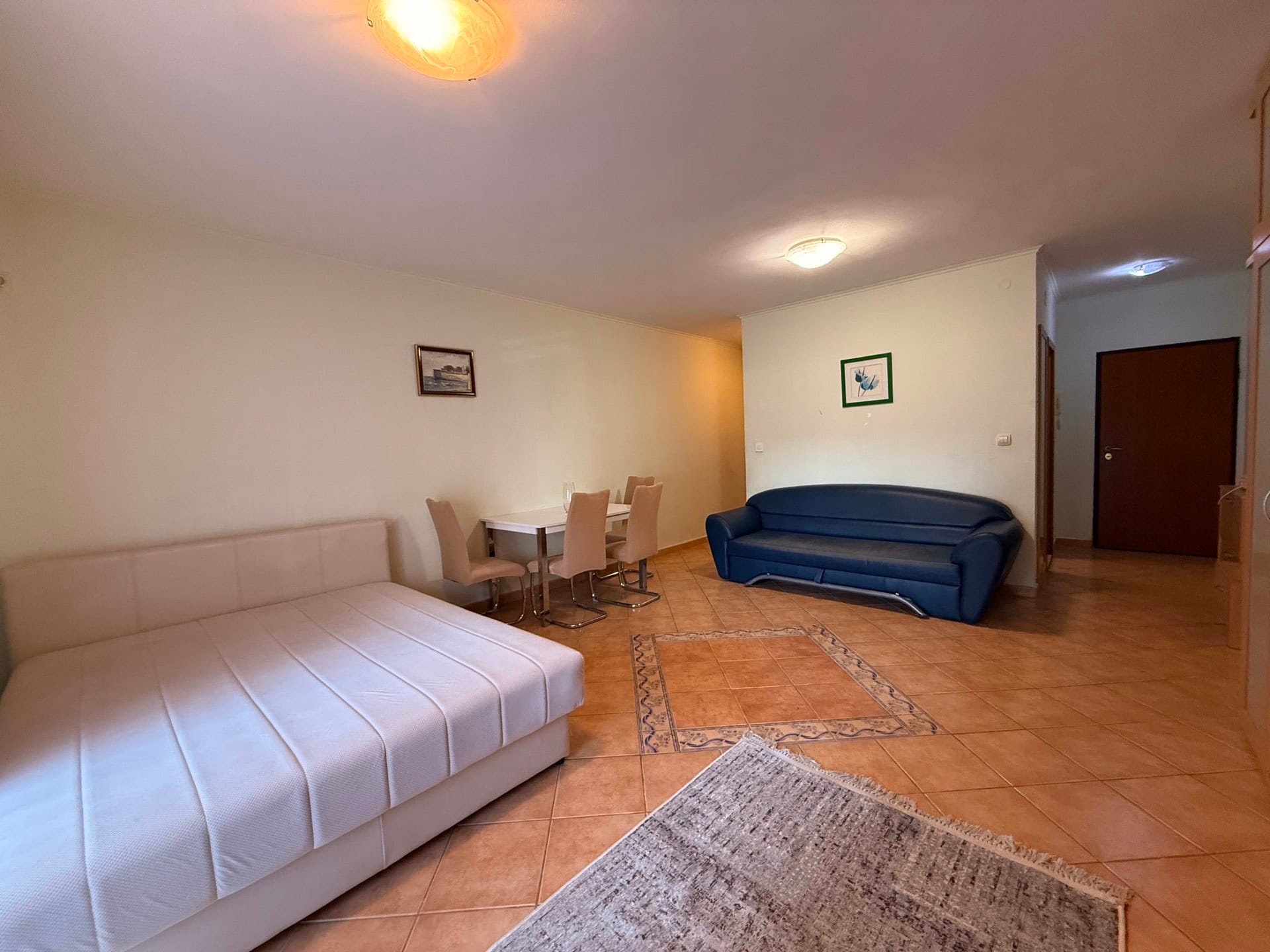 Living room in an apartment in Budva, Montenegro: double bed, blue sofa, dining area, and tiled floor.