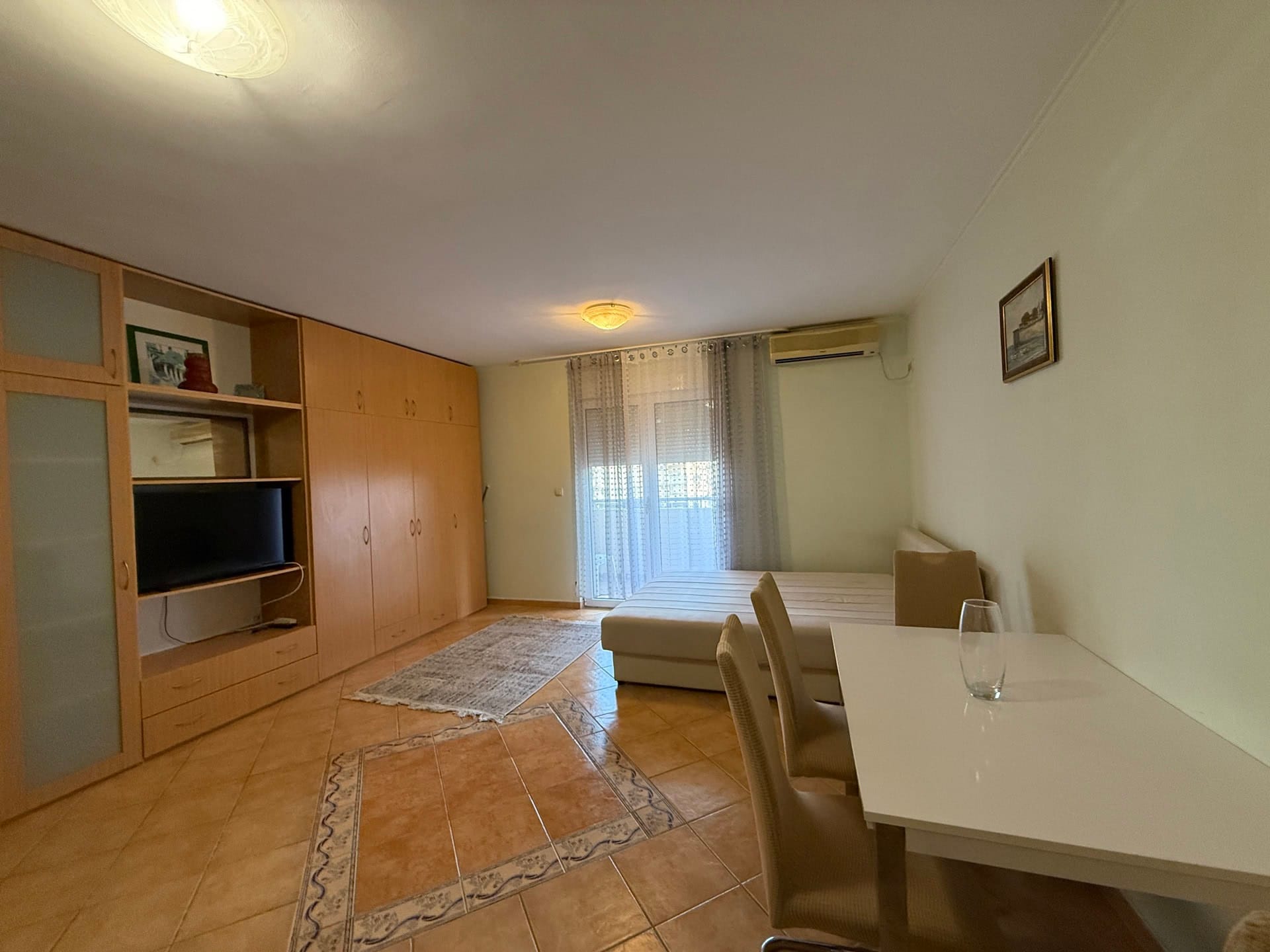 Living room in an apartment in Budva, Montenegro: a bright room with furniture, a dining area, tile flooring, and access to the balcony.