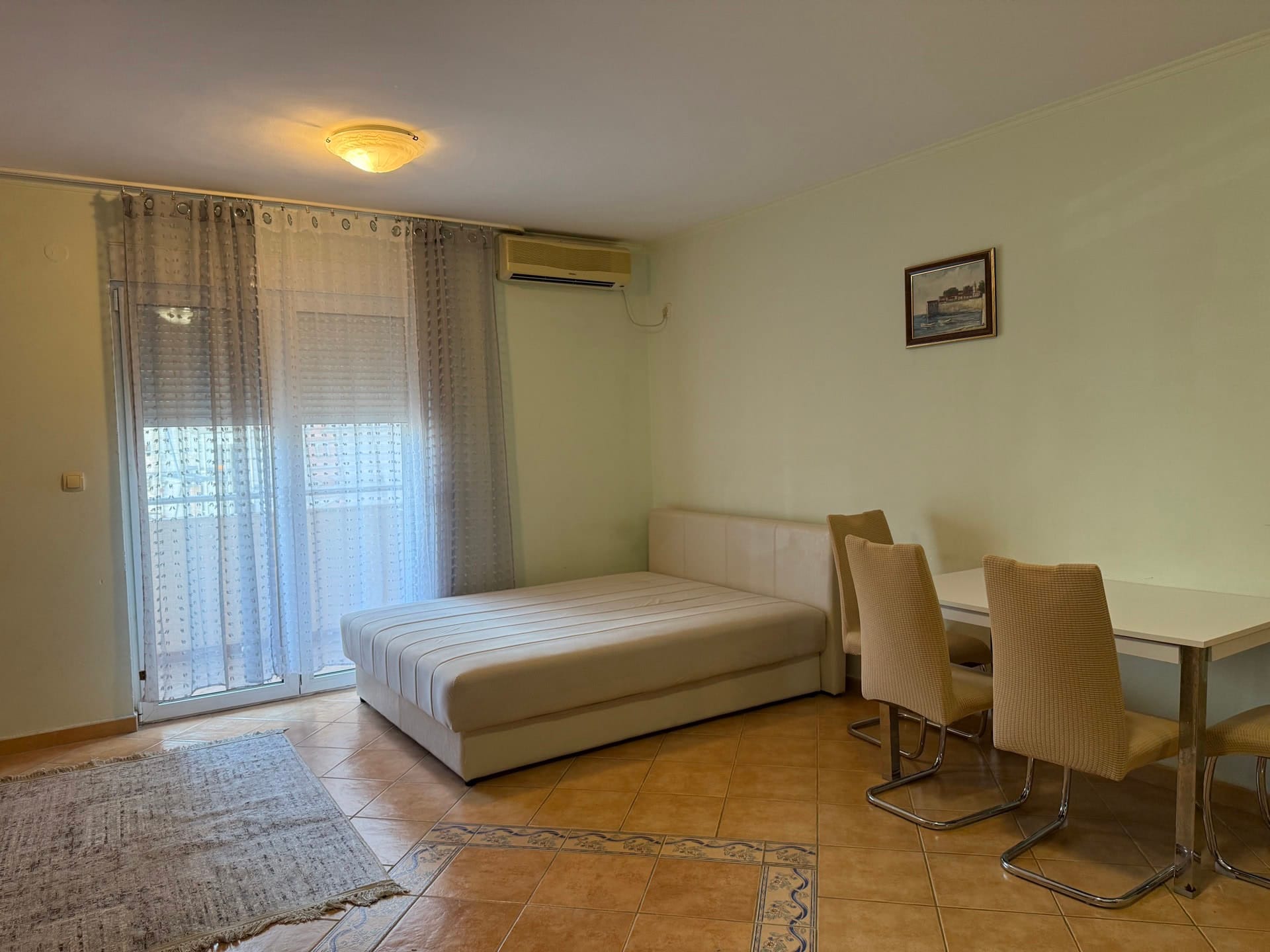 Bright living room in an apartment in Budva, Montenegro: double bed, dining area, tiled floor, and access to the balcony.