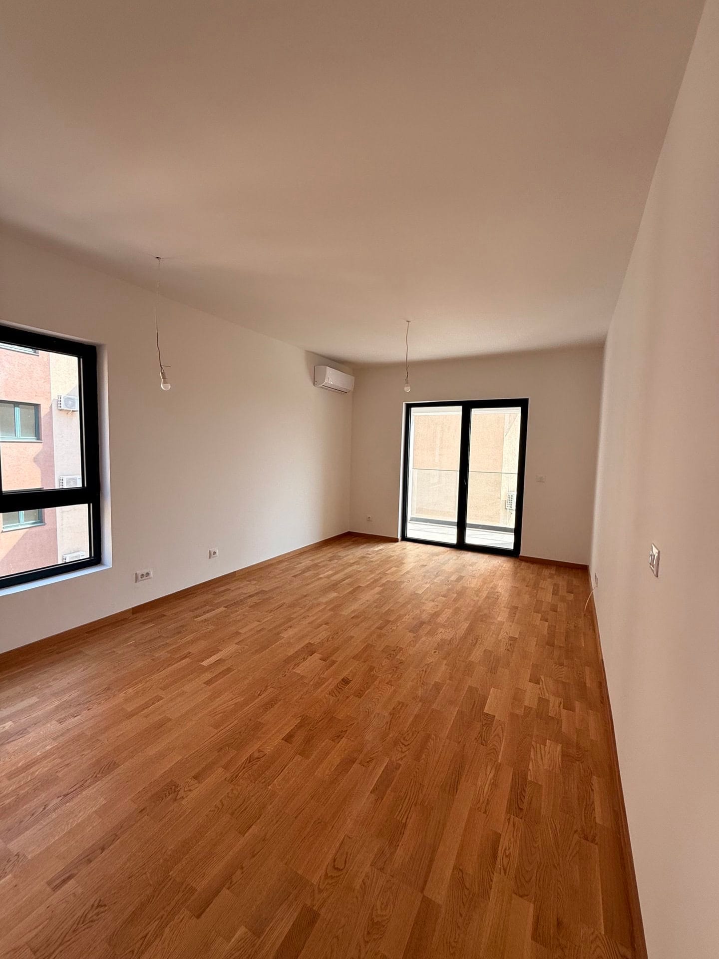 Svetla dnevna soba sa parketom i izlazom na balkon u novom stanu, Bečići, Crna Gora.
