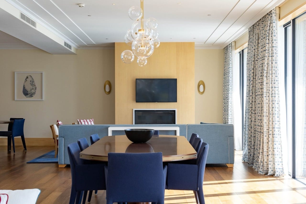 Nowoczesny salon z jadalnią w apartamencie w Tivacie, Czarnogóra: niebieskie fotele, kominek i designerski żyrandol.