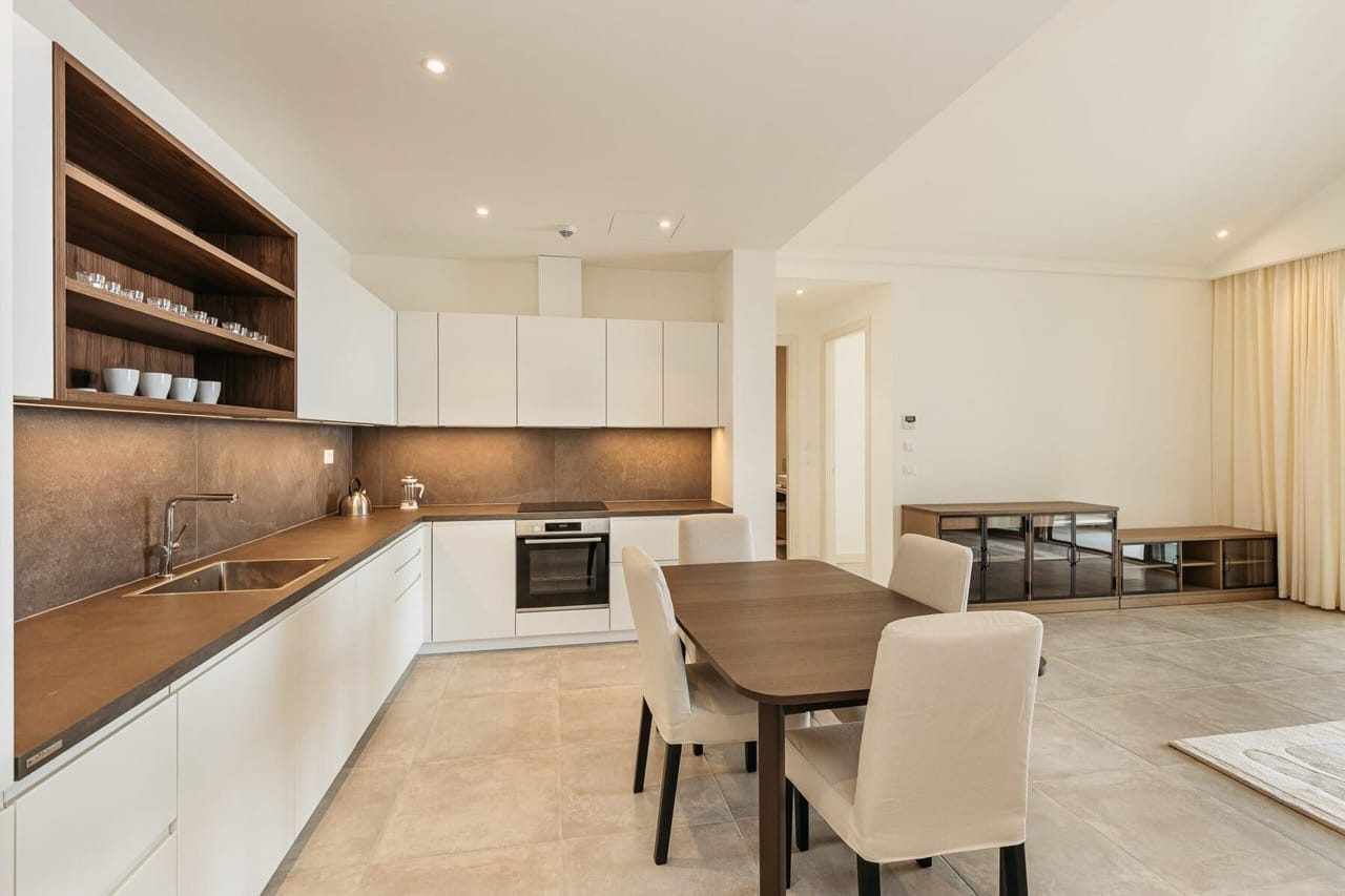 Modern kitchen with dining area in an apartment in Luštica Bay, Radovići, Montenegro: white fronts and dark wood.