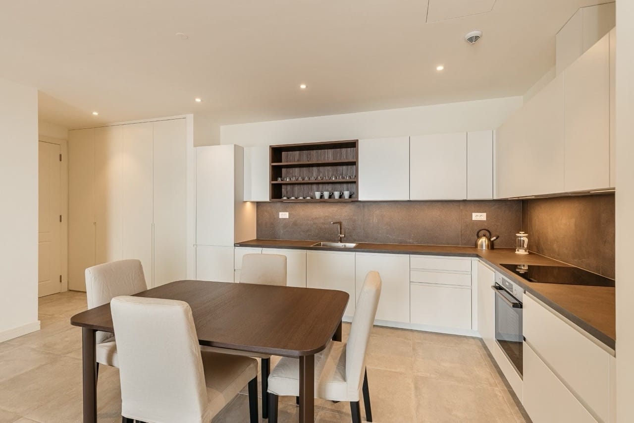 Modern kitchen in an apartment in Luštica Bay, Radovići, Montenegro: light cabinetry, dark countertop, and dining area.